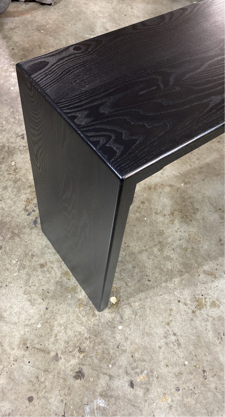 A black waterfall console table made of solid wood, showing the grain and the sleek, smooth finish.